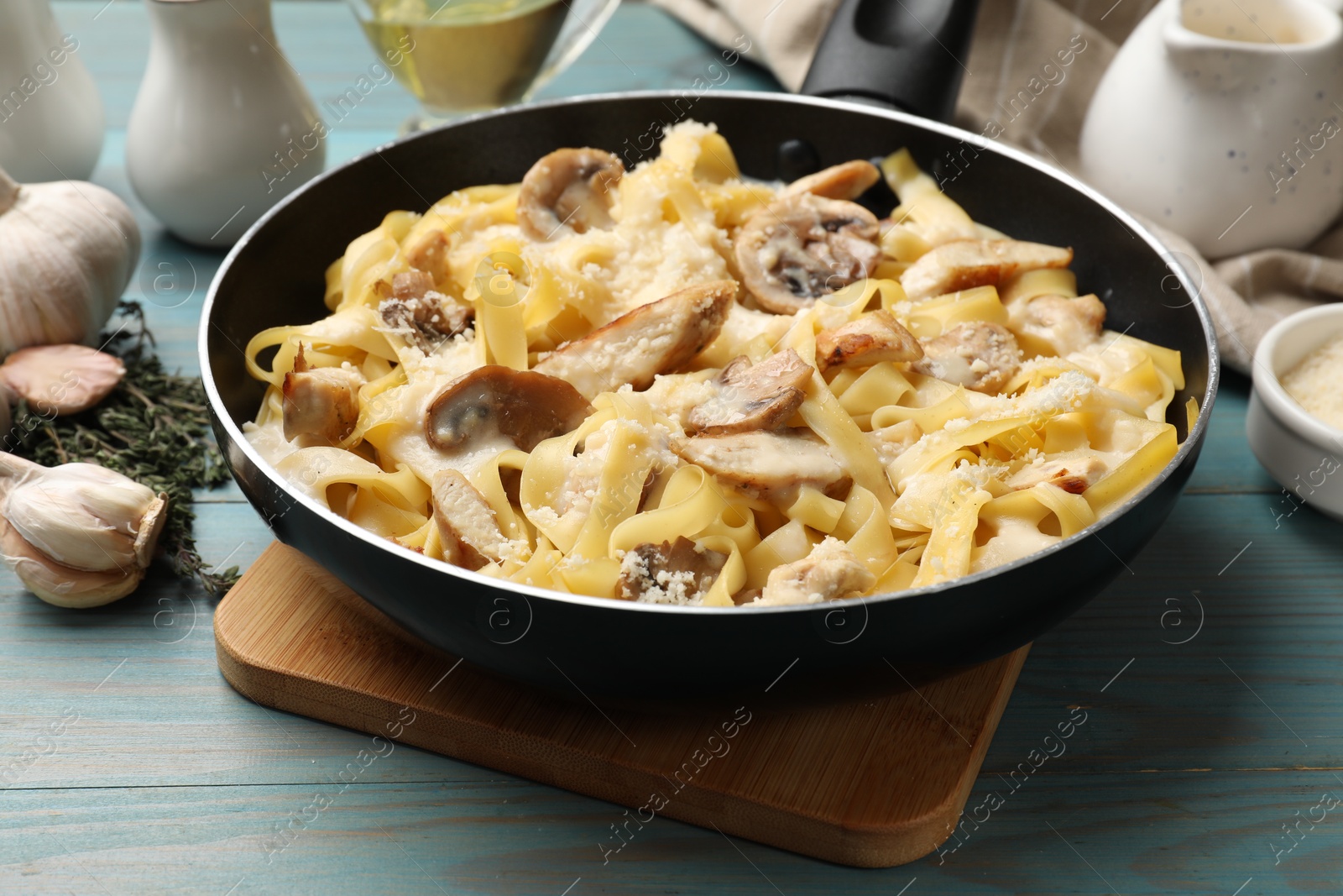 Photo of Tasty Alfredo pasta with chicken and mushrooms in frying pan on light blue wooden table, closeup