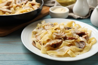 Photo of Tasty Alfredo pasta with chicken and mushrooms on light blue wooden table, closeup