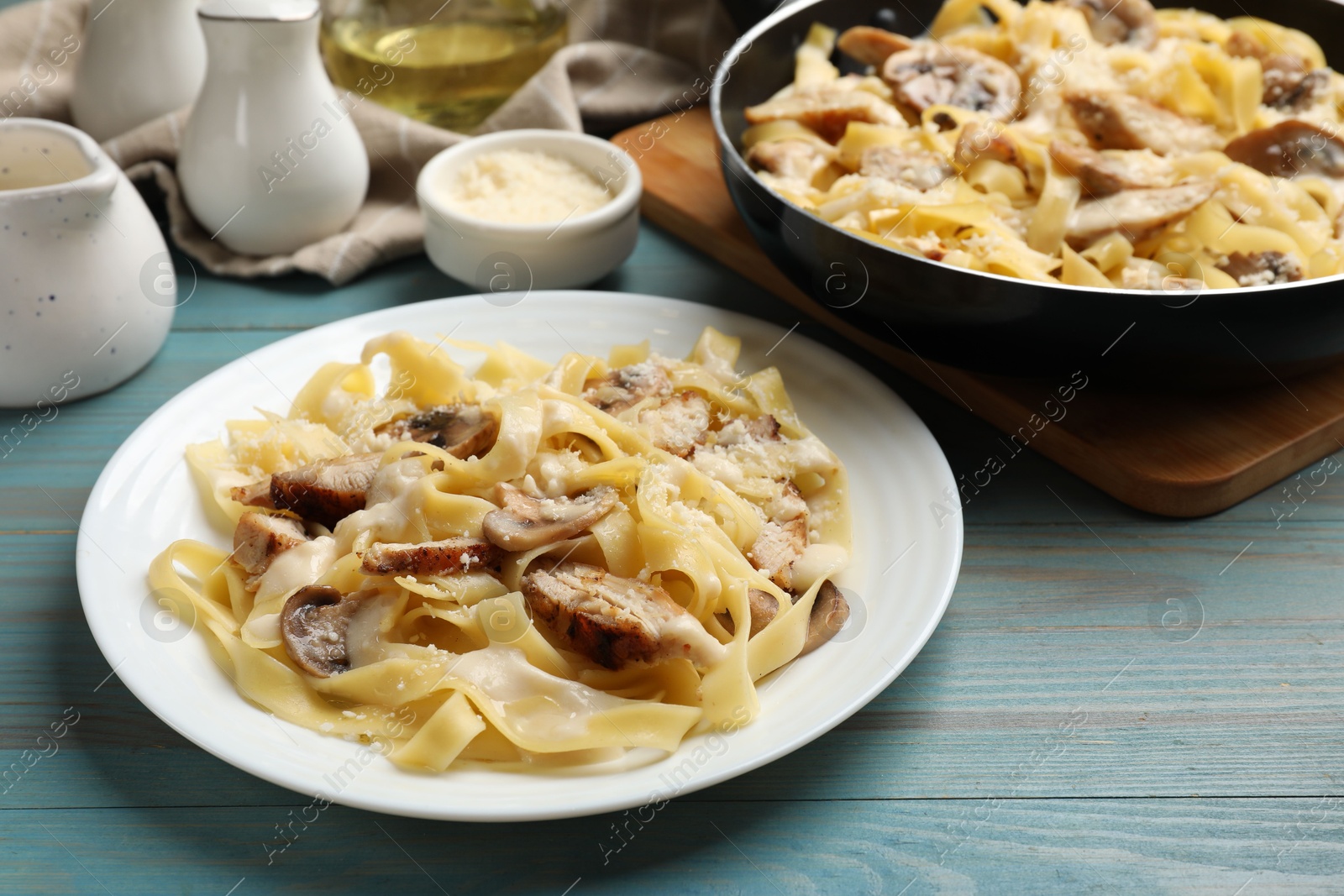 Photo of Tasty Alfredo pasta with chicken and mushrooms on light blue wooden table, closeup