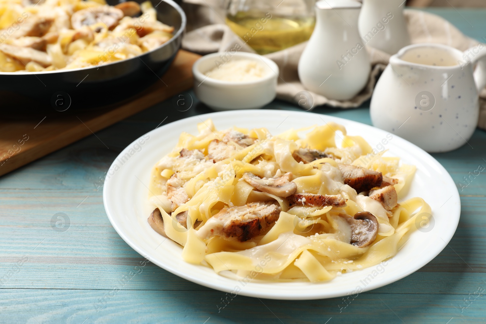 Photo of Tasty Alfredo pasta with chicken and mushrooms on light blue wooden table, closeup