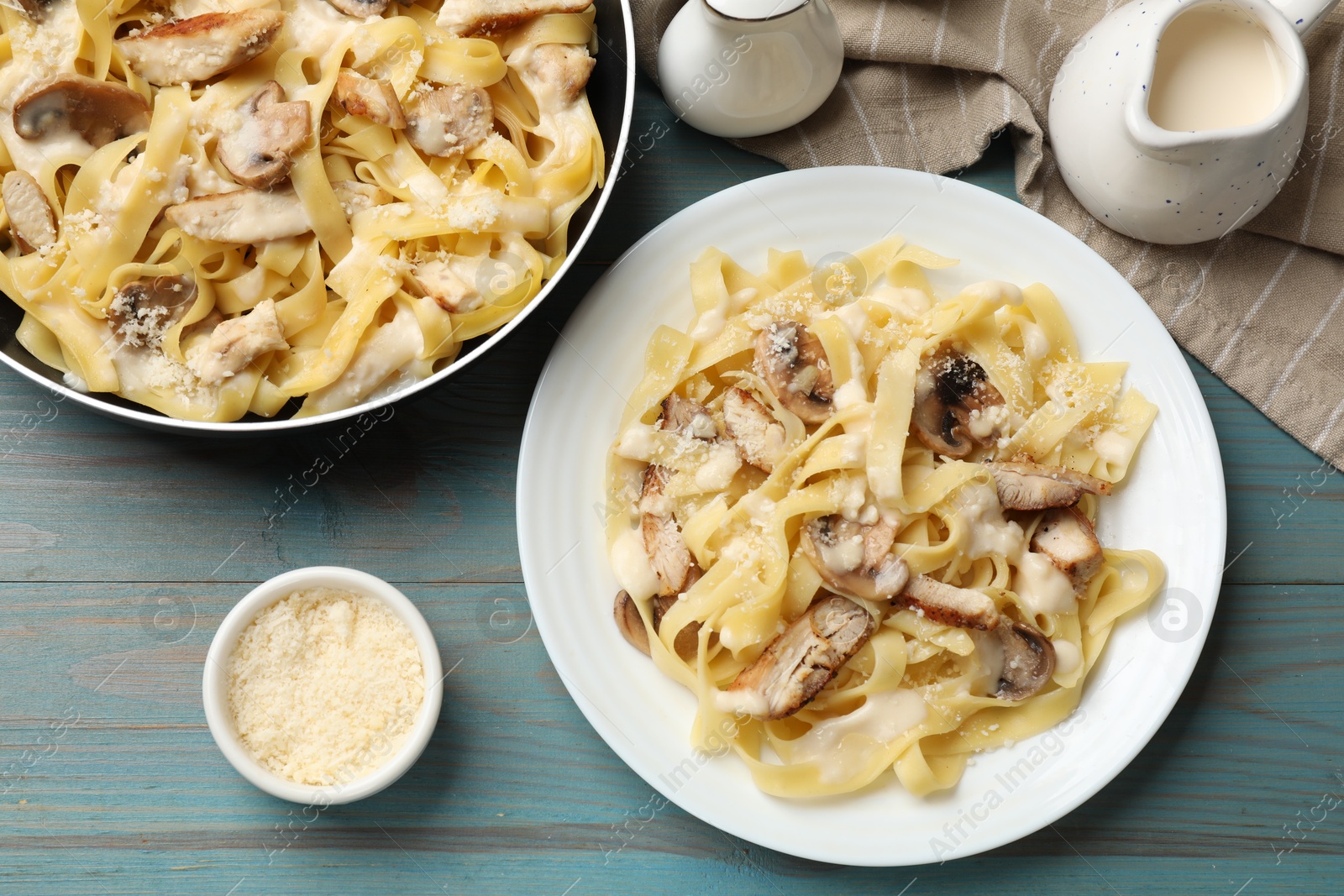 Photo of Tasty Alfredo pasta with chicken, mushrooms, cheese and creamy sauce on light blue wooden table, flat lay