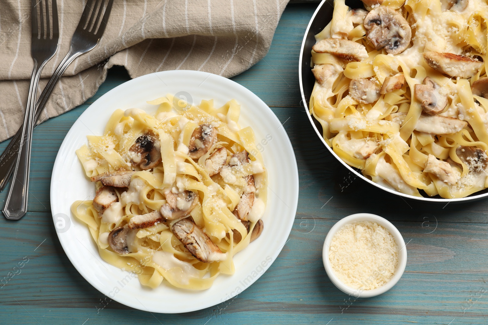 Photo of Tasty Alfredo pasta with chicken served on light blue wooden table, flat lay