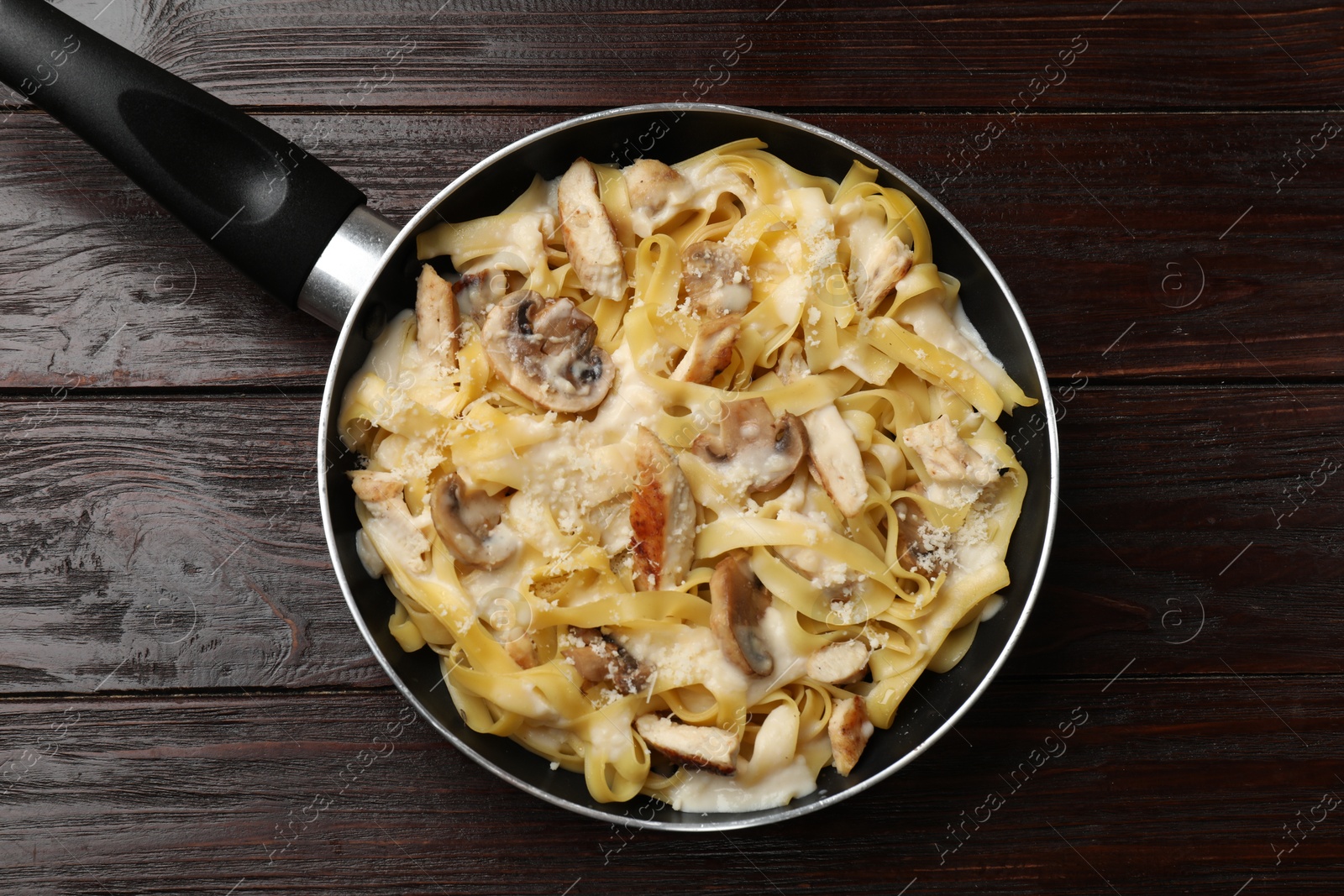 Photo of Tasty Alfredo pasta with chicken and mushrooms in frying pan on wooden table, top view