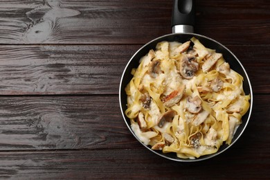 Photo of Tasty Alfredo pasta with chicken and mushrooms in frying pan on wooden table, top view. Space for text