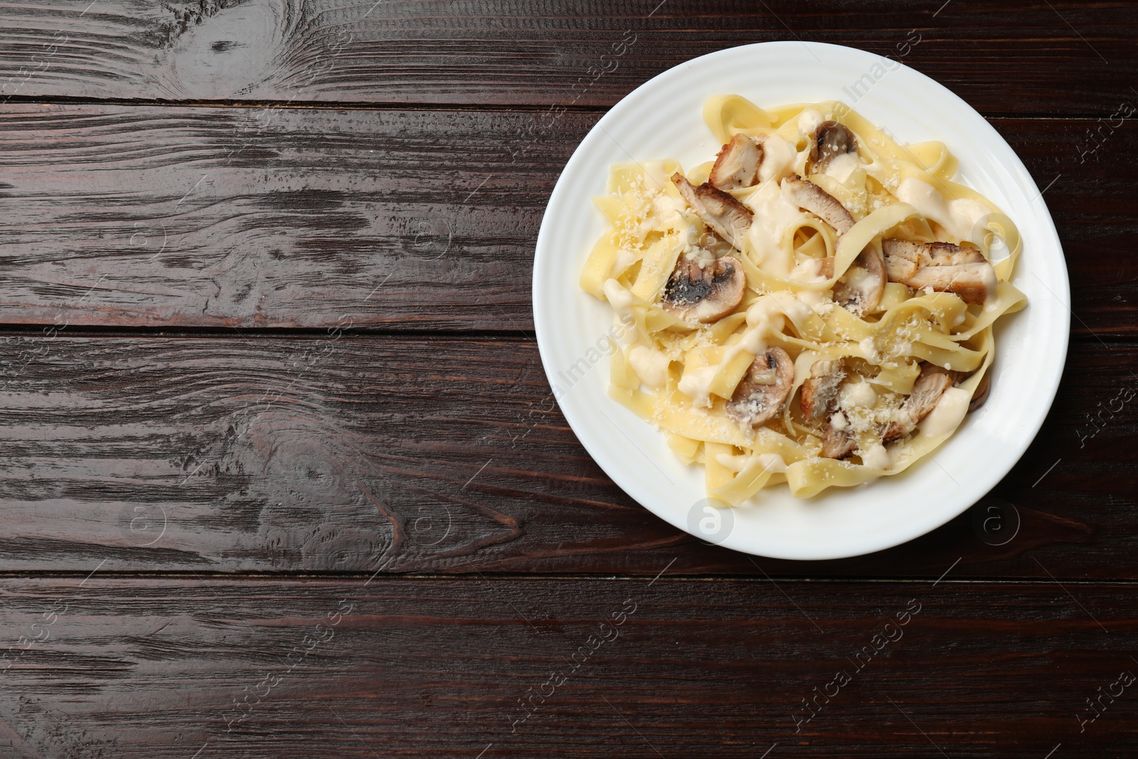 Photo of Tasty Alfredo pasta with chicken and mushrooms on wooden table, top view. Space for text