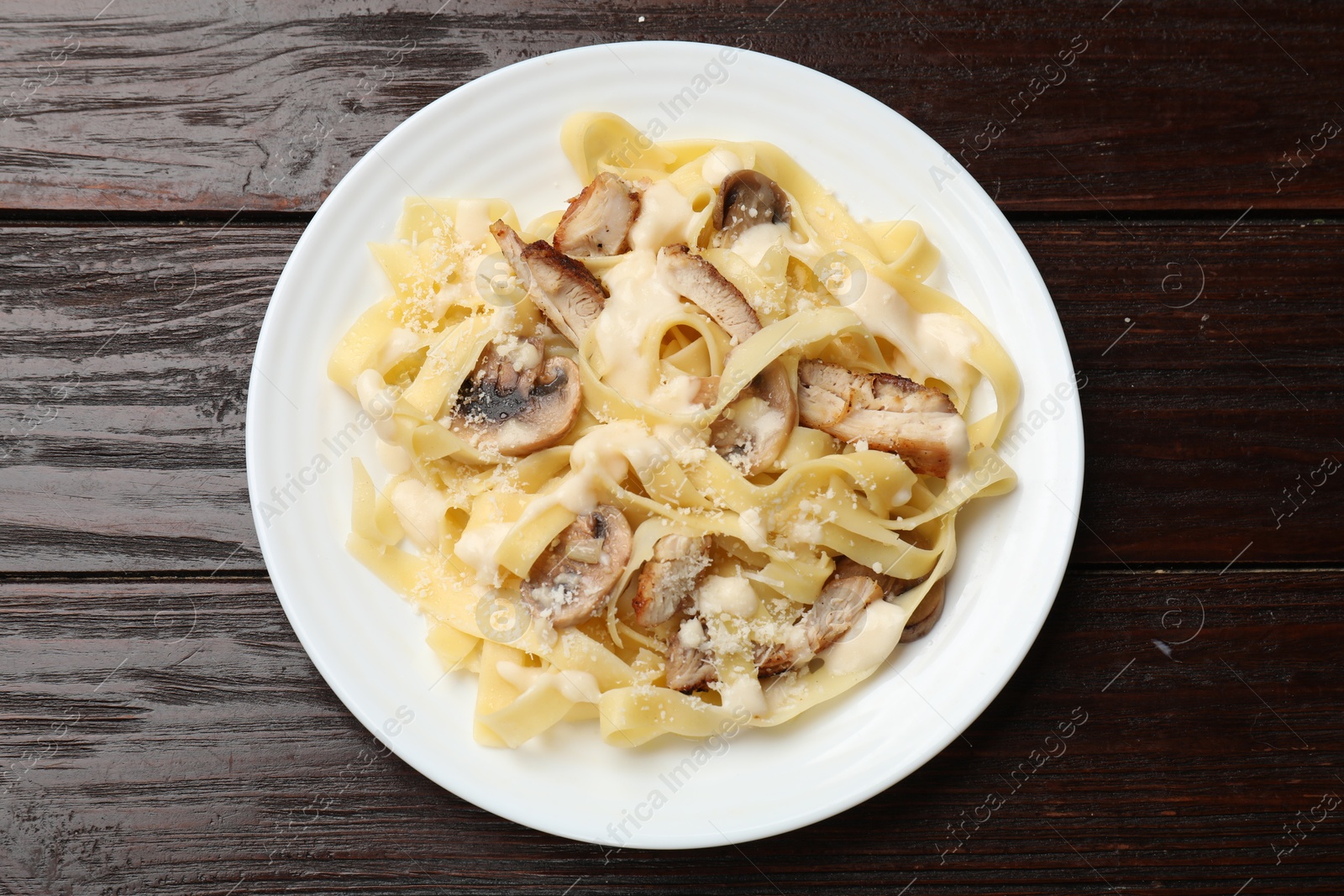 Photo of Tasty Alfredo pasta with chicken and mushrooms on wooden table, top view