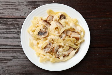 Photo of Tasty Alfredo pasta with chicken and mushrooms on wooden table, top view