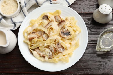 Photo of Tasty Alfredo pasta with chicken, mushrooms, cheese and creamy sauce on wooden table, flat lay