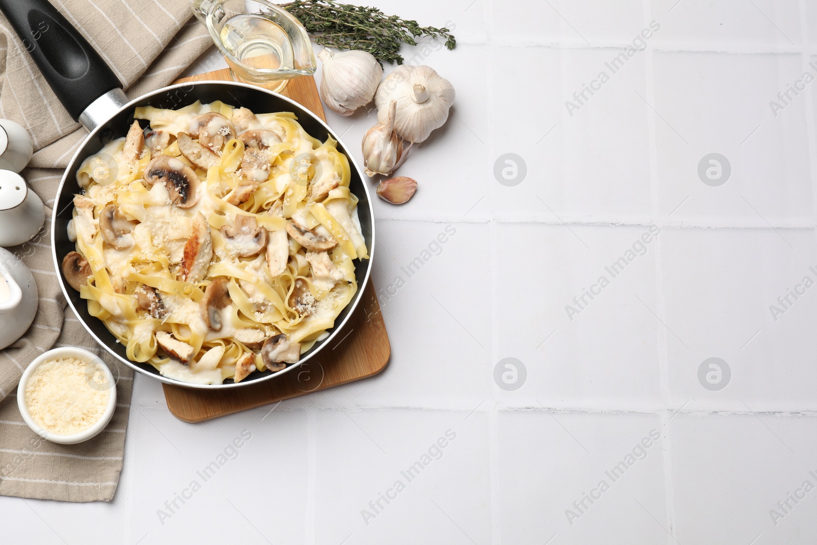 Photo of Flat lay composition with tasty Alfredo pasta with chicken and mushrooms on white tiled table, space for text