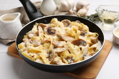 Photo of Tasty Alfredo pasta with chicken and mushrooms in frying pan on light table, closeup