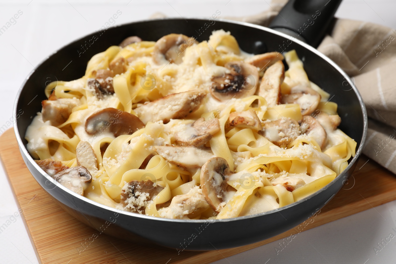 Photo of Tasty Alfredo pasta with chicken and mushrooms in frying pan on light table, closeup