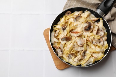 Photo of Tasty Alfredo pasta with chicken and mushrooms in frying pan on white tiled table, top view. Space for text