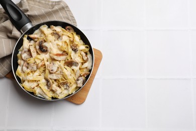 Photo of Tasty Alfredo pasta with chicken and mushrooms in frying pan on white tiled table, top view. Space for text