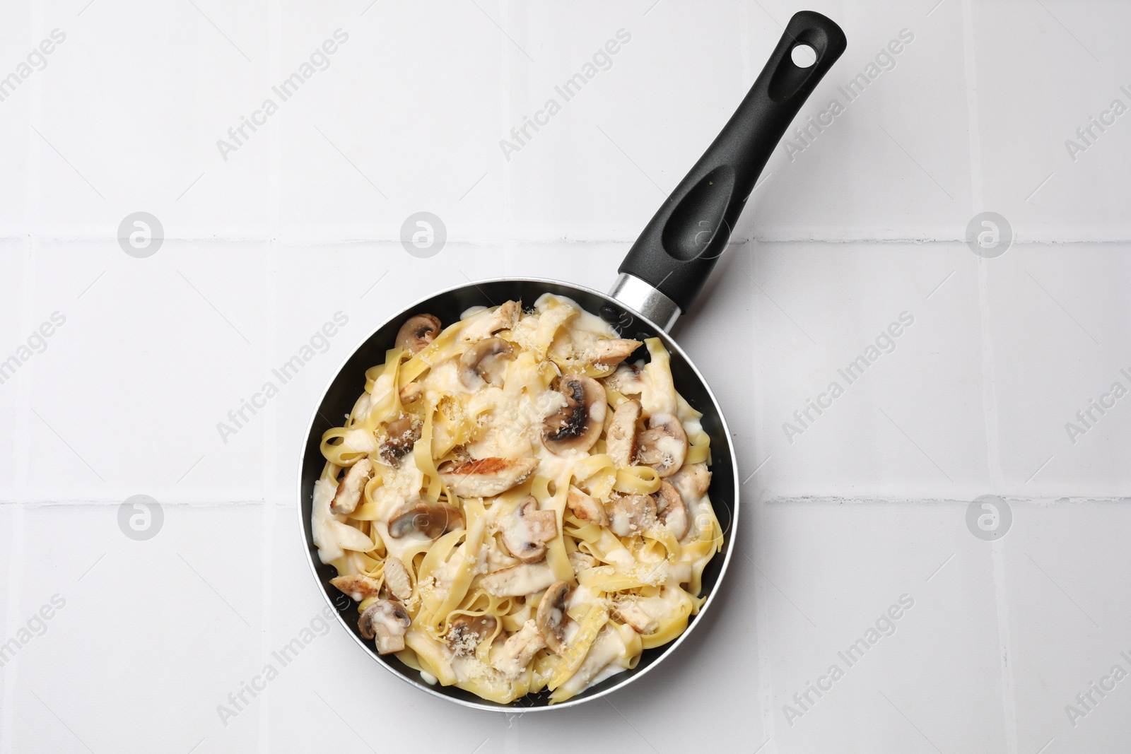 Photo of Tasty Alfredo pasta with chicken and mushrooms in frying pan on white tiled table, top view