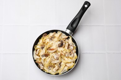 Photo of Tasty Alfredo pasta with chicken and mushrooms in frying pan on white tiled table, top view