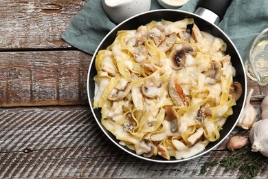 Photo of Flat lay composition with tasty Alfredo pasta with chicken and mushrooms in frying pan on wooden table, space for text