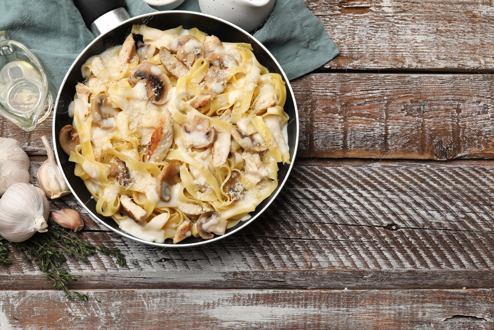 Photo of Flat lay composition with tasty Alfredo pasta with chicken and mushrooms in frying pan on wooden table, space for text