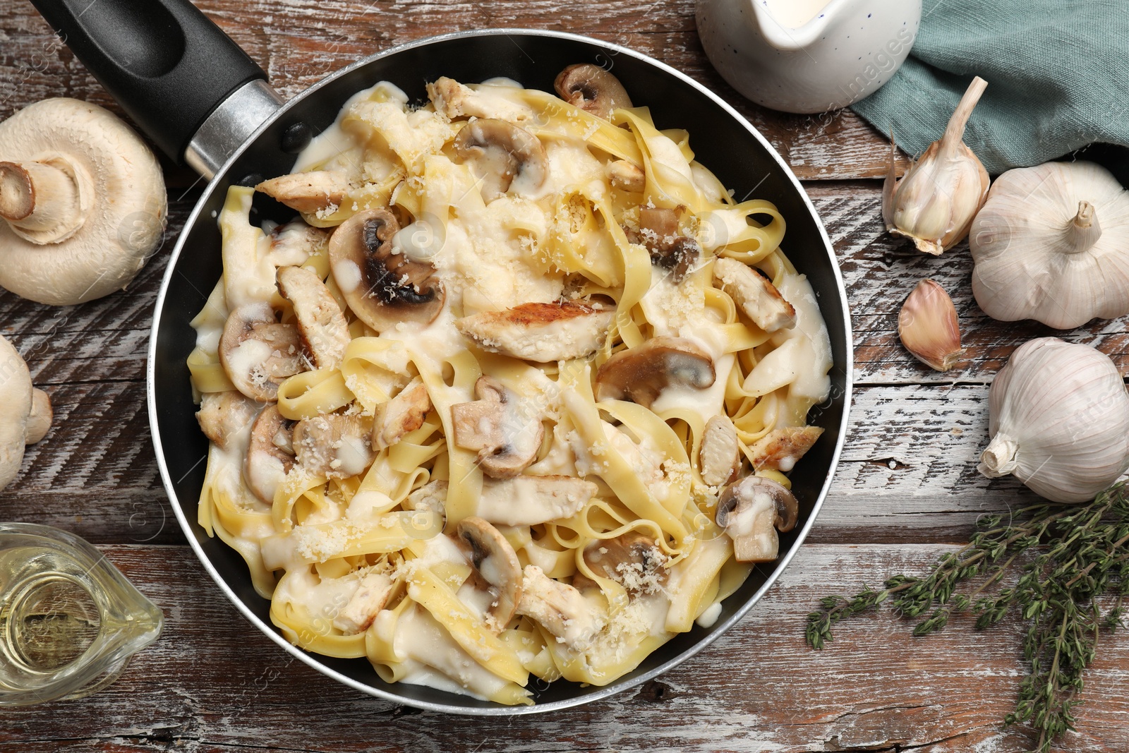 Photo of Flat lay composition with tasty Alfredo pasta with chicken and mushrooms in frying pan on wooden table