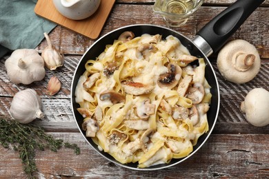 Photo of Flat lay composition with tasty Alfredo pasta with chicken and mushrooms in frying pan on wooden table