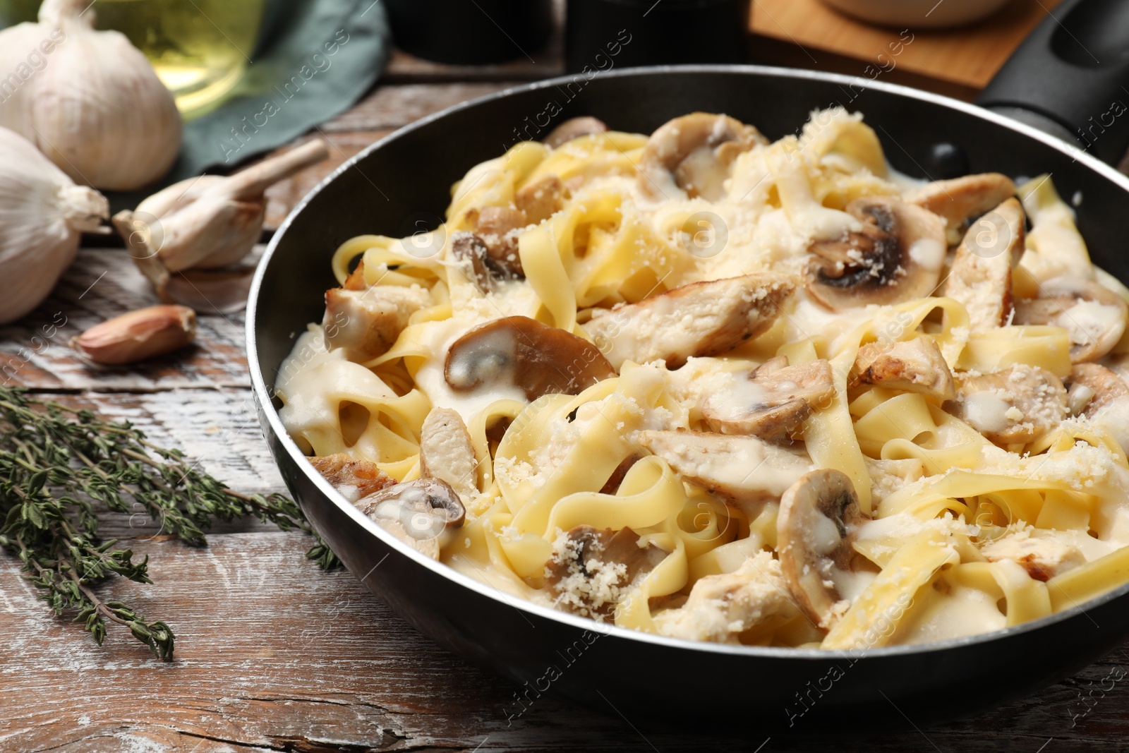 Photo of Tasty Alfredo pasta with chicken and mushrooms in frying pan on wooden table, closeup