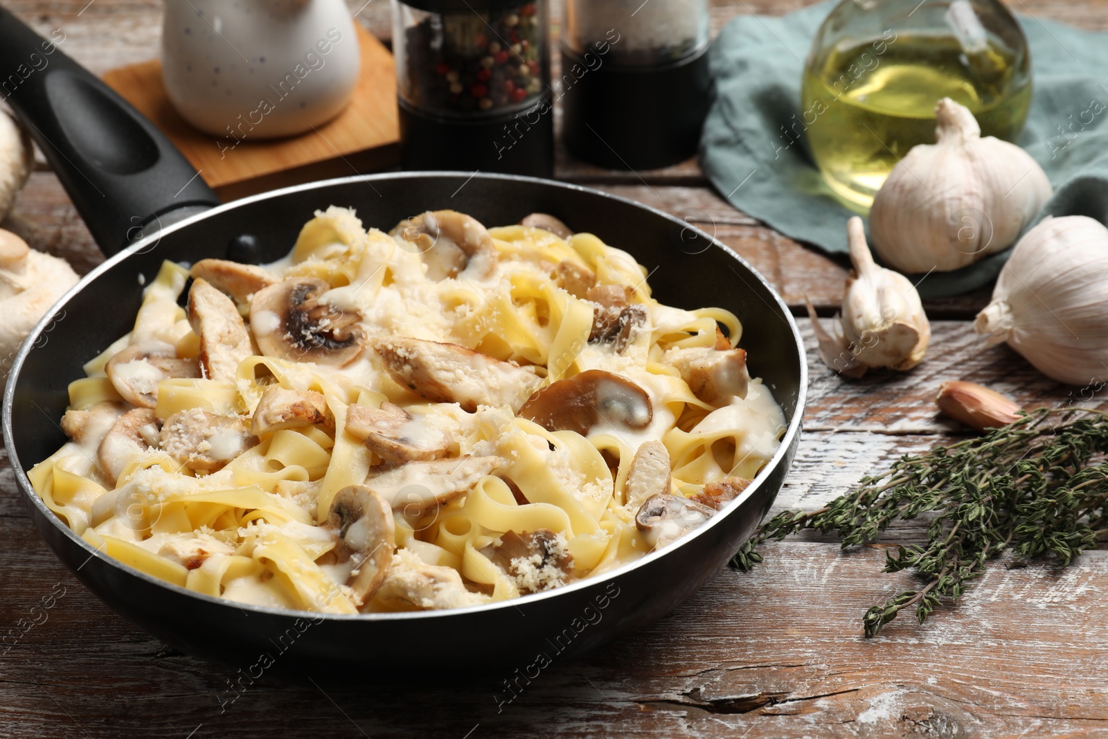 Photo of Tasty Alfredo pasta with chicken and mushrooms in frying pan on wooden table, closeup