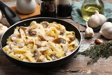 Photo of Tasty Alfredo pasta with chicken and mushrooms in frying pan on wooden table, closeup