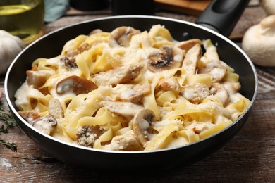 Photo of Tasty Alfredo pasta with chicken and mushrooms in frying pan on wooden table, closeup