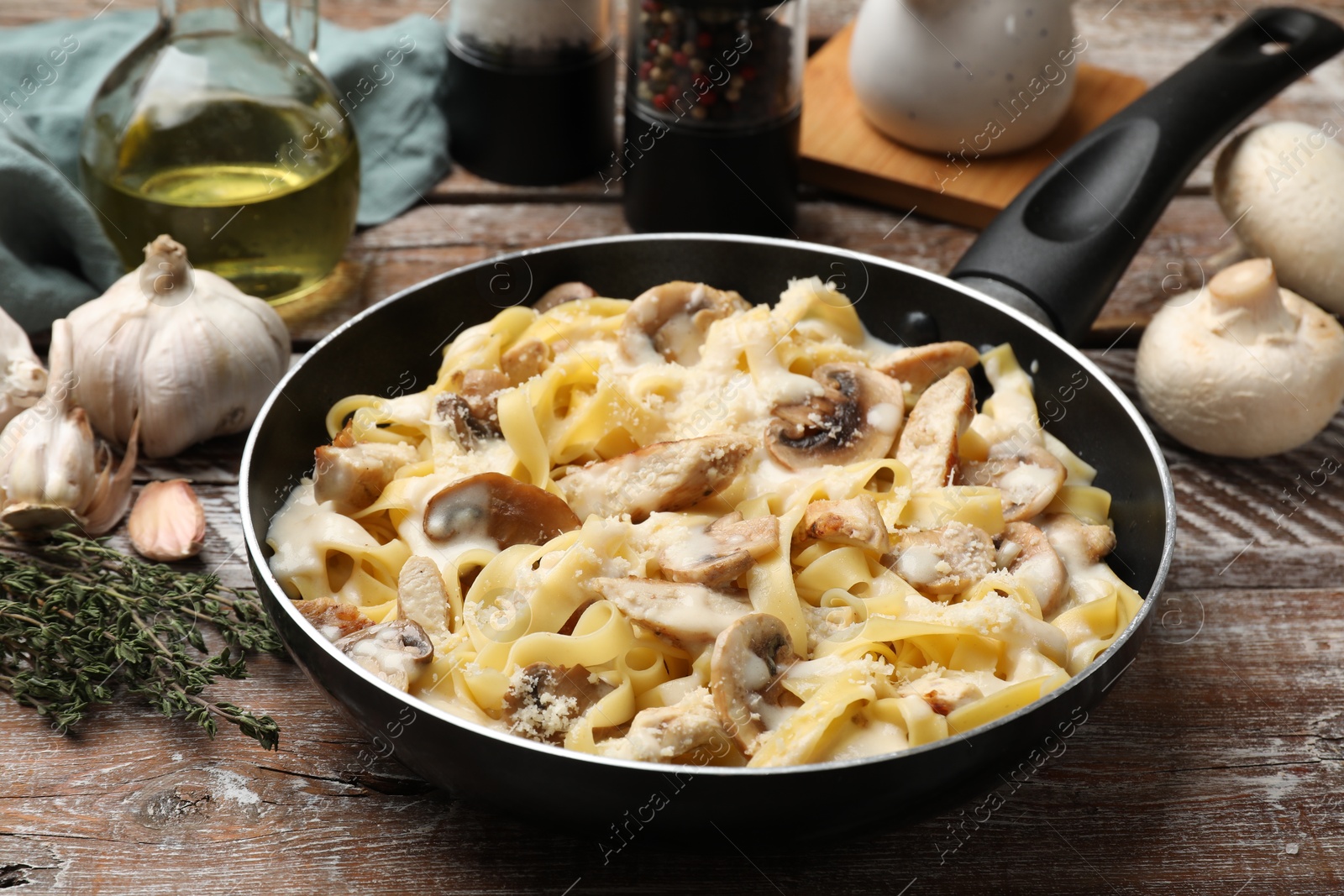 Photo of Tasty Alfredo pasta with chicken and mushrooms in frying pan on wooden table, closeup