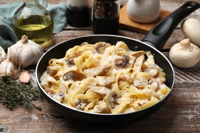 Photo of Tasty Alfredo pasta with chicken and mushrooms in frying pan on wooden table, closeup