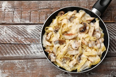 Photo of Tasty Alfredo pasta with chicken and mushrooms in frying pan on wooden table, top view. Space for text