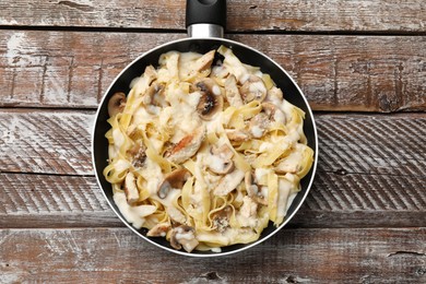 Photo of Tasty Alfredo pasta with chicken and mushrooms in frying pan on wooden table, top view