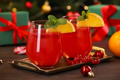 Photo of Christmas cocktail in glasses with lemon and currants on wooden table, closeup