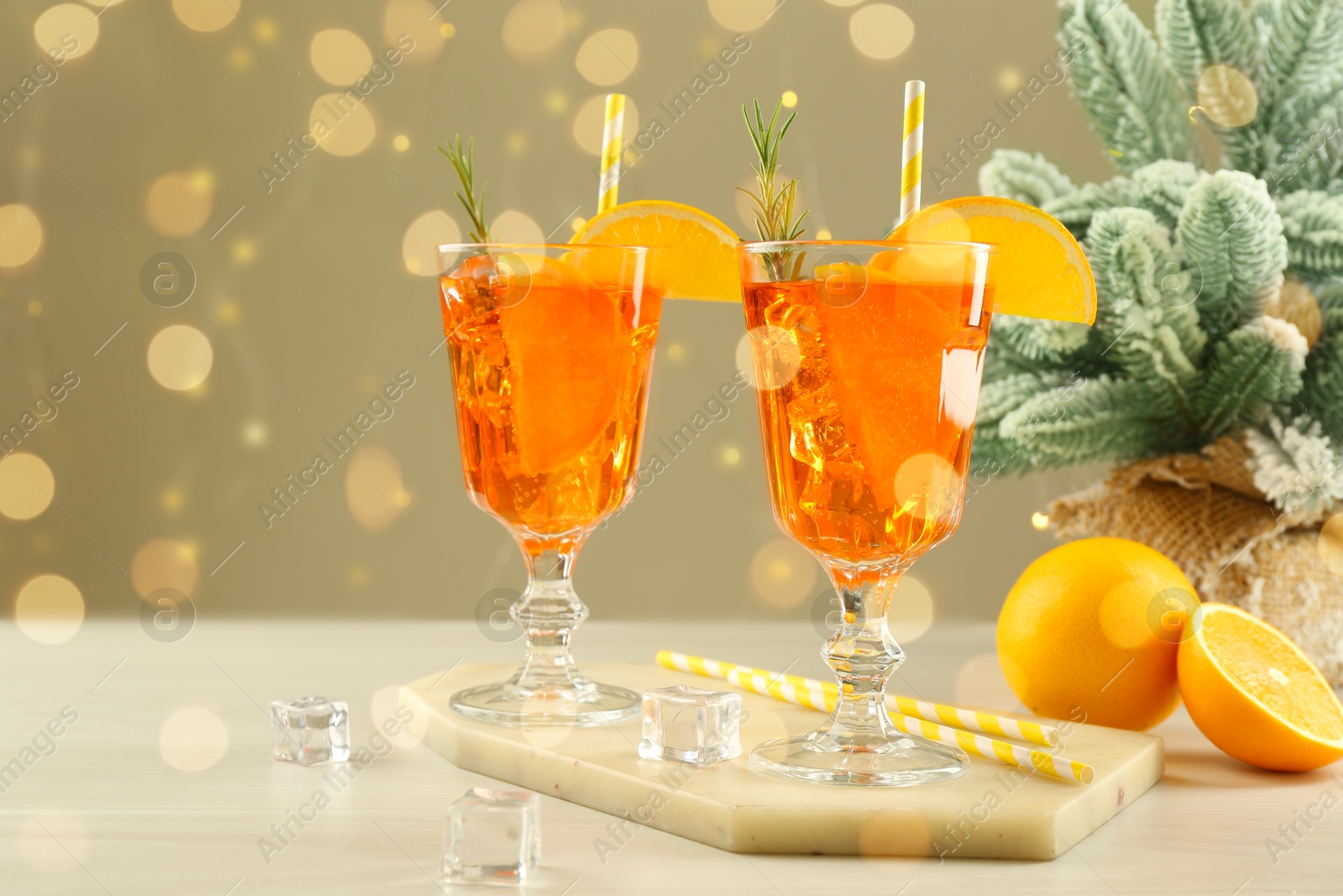 Photo of Tasty Christmas cocktail in glasses and fir tree branches on white wooden table against blurred lights