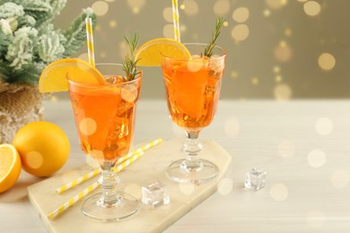 Photo of Tasty Christmas cocktail in glasses and fir tree branches on white wooden table against blurred lights