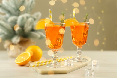 Photo of Tasty Christmas cocktail in glasses and fir tree branches on white wooden table against blurred lights