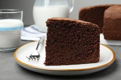 Photo of Piece of tasty chocolate sponge cake served on grey table, closeup