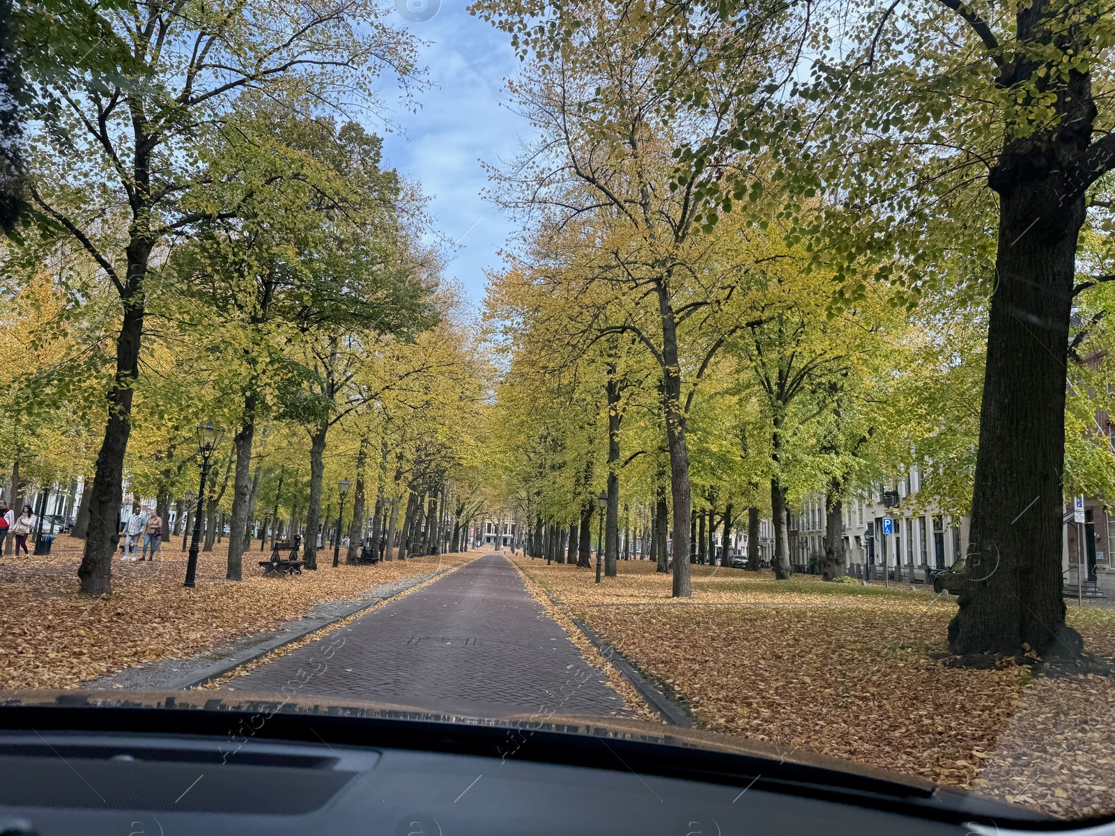 Photo of Beautiful alley with colorful trees and pathway in autumn park, view through car windshield