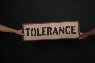 Image of Woman and African American man holding sign with word Tolerance on black background, closeup