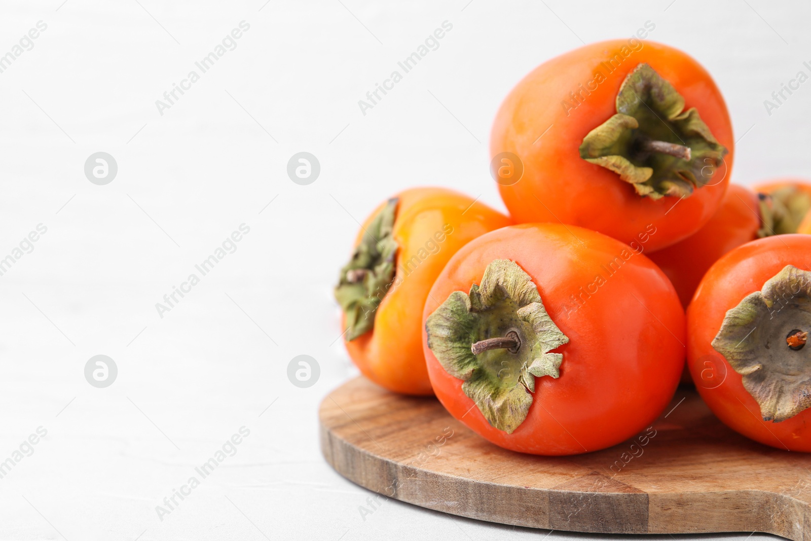 Photo of Delicious fresh juicy persimmons on white table, closeup. Space for text