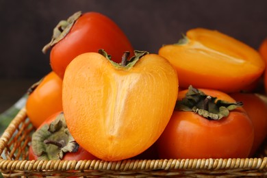 Whole and cut juicy persimmons in wicker basket on brown background, closeup