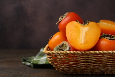 Whole and cut juicy persimmons in wicker basket on wooden table, closeup. Space for text