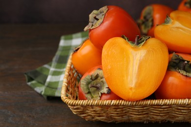 Whole and cut juicy persimmons in wicker basket on wooden table, closeup. Space for text