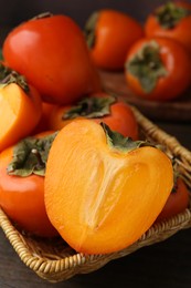 Whole and cut fresh persimmons in wicker basket on wooden table, closeup