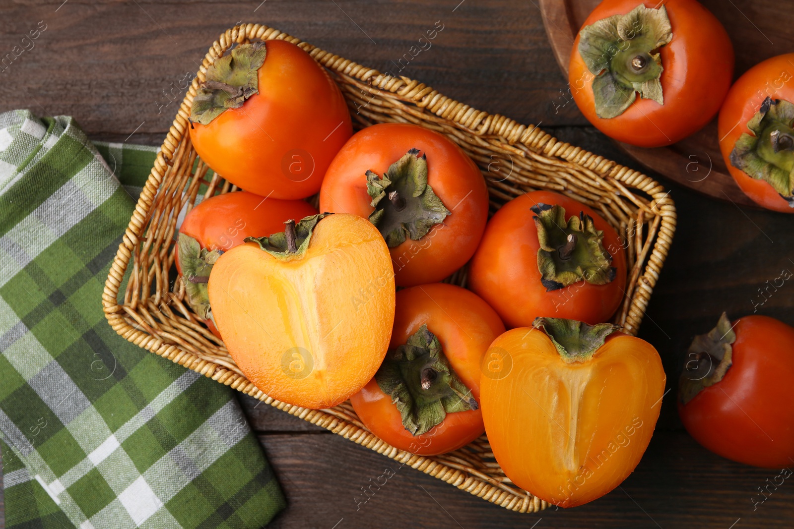 Photo of Delicious fresh juicy persimmons in wicker basket on wooden table, top view