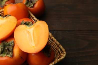 Photo of Delicious fresh juicy persimmons in wicker basket on wooden table, closeup. Space for text