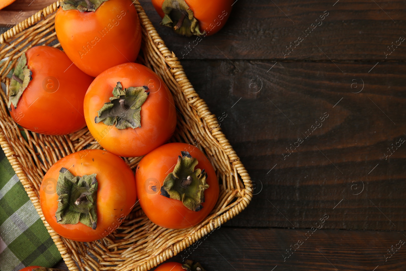 Photo of Delicious fresh juicy persimmons in wicker basket on wooden table, top view. Space for text