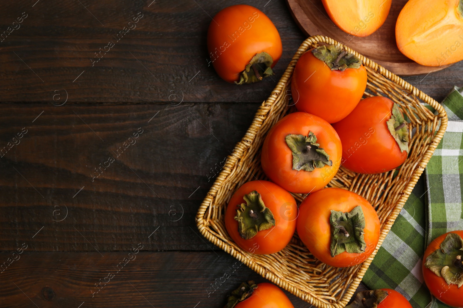 Photo of Delicious fresh juicy persimmons in wicker basket on wooden table, top view. Space for text