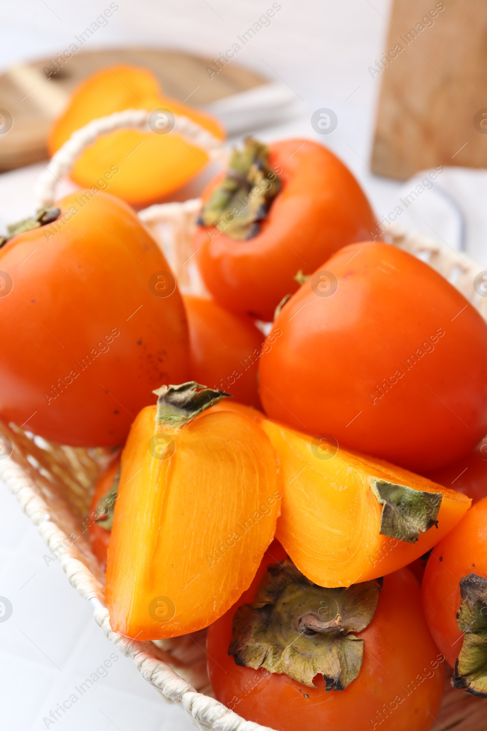 Photo of Ripe persimmons in wicker basket on white table, closeup