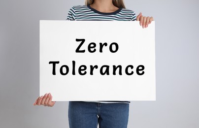 Image of Woman holding poster with words Zero Tolerance on light grey background, closeup