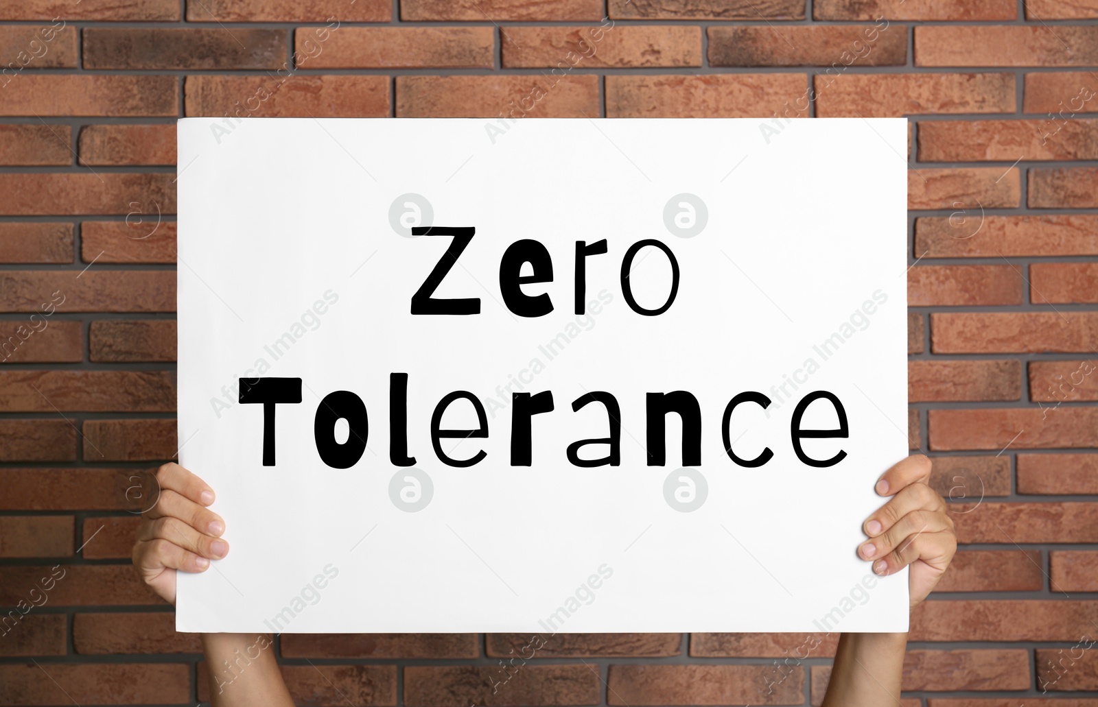 Image of Man holding poster with words Zero Tolerance near red brick wall, closeup